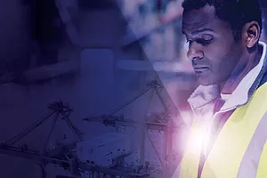 A MAN IN A HI-VIS VEST PEERS INTO A TABLET COMPUTER, SURROUNDED BY IMAGES OF PORT CRANES