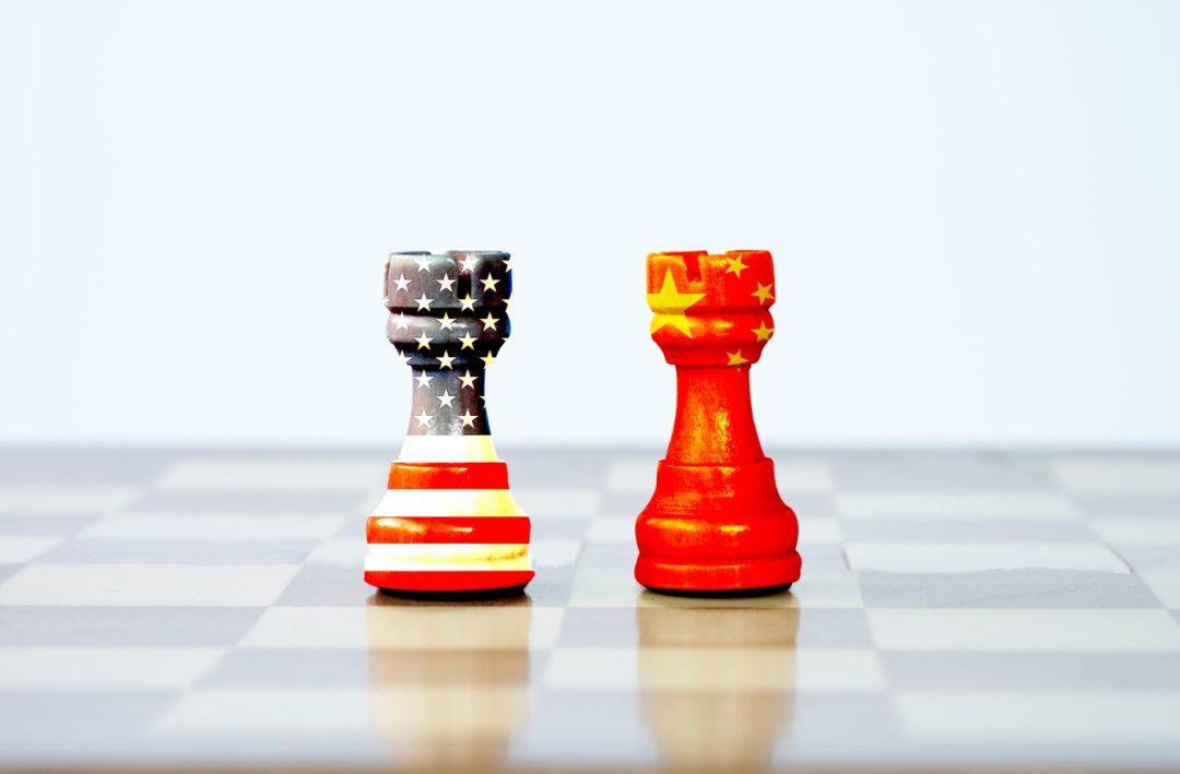 TWO CHESS PIECES COLORED WITH US AND CHINA FLAGS CONFRONT EACH OTHER ON A BOARD
