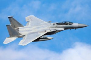 AN F-15 FIGHTER JET FLIES ACROSS A CLOUD-FLECKED BLUE SKY