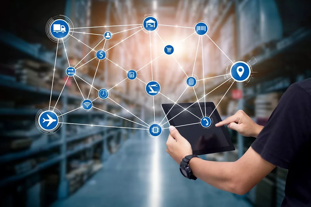 A PERSON HOLDING A TABLET COMPUTER CASTS AN IMAGINARY WEB OF CONNECTIONS ACROSS A WAREHOUSE AISLE