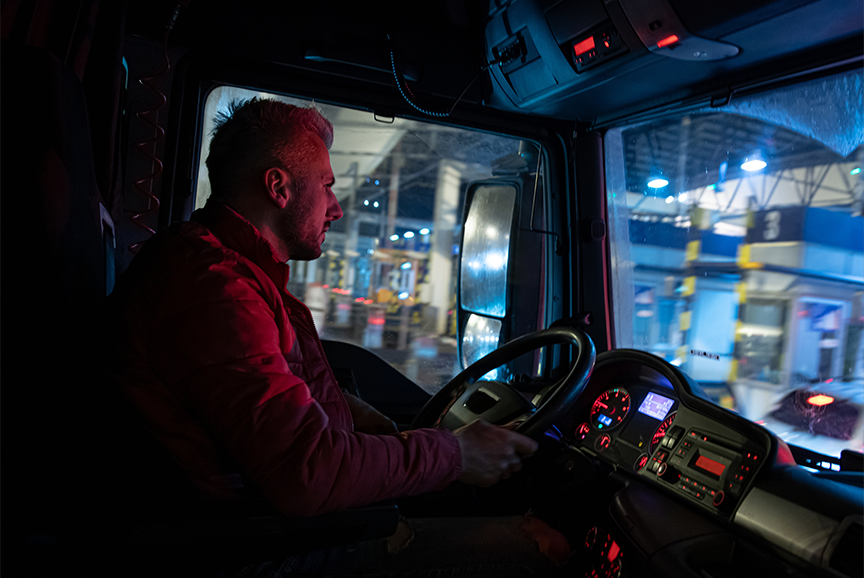 A TRUCK DRIVER SITS IN A DIMLY LIT CAB AT NIGHT