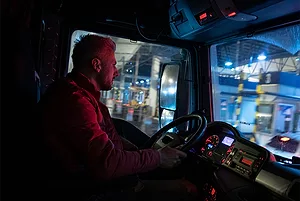 A TRUCK DRIVER SITS IN A DIMLY LIT CAB AT NIGHT