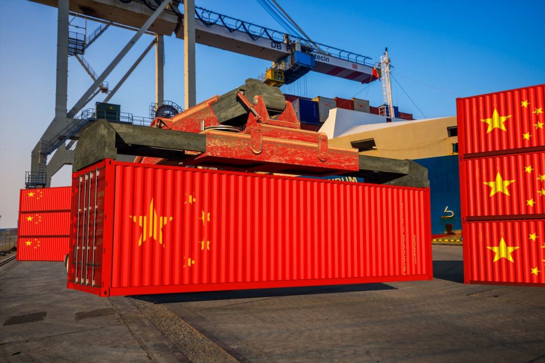 CONTAINERS BEARING THE CHINESE FLAG SIT AT A DOCK UNDER CRANES