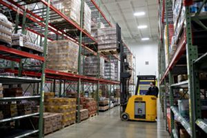  A WORKER OPERATES A FORKLIFT IN AN AISLE OF A WAREHOUSE