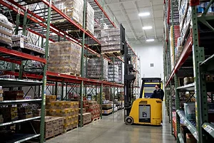  A WORKER OPERATES A FORKLIFT IN AN AISLE OF A WAREHOUSE