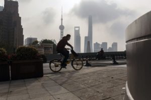 A BICYCLIST RIDES ALONG WITH THE SHANGHAI SKYLINE IN THE BACKGROUND
