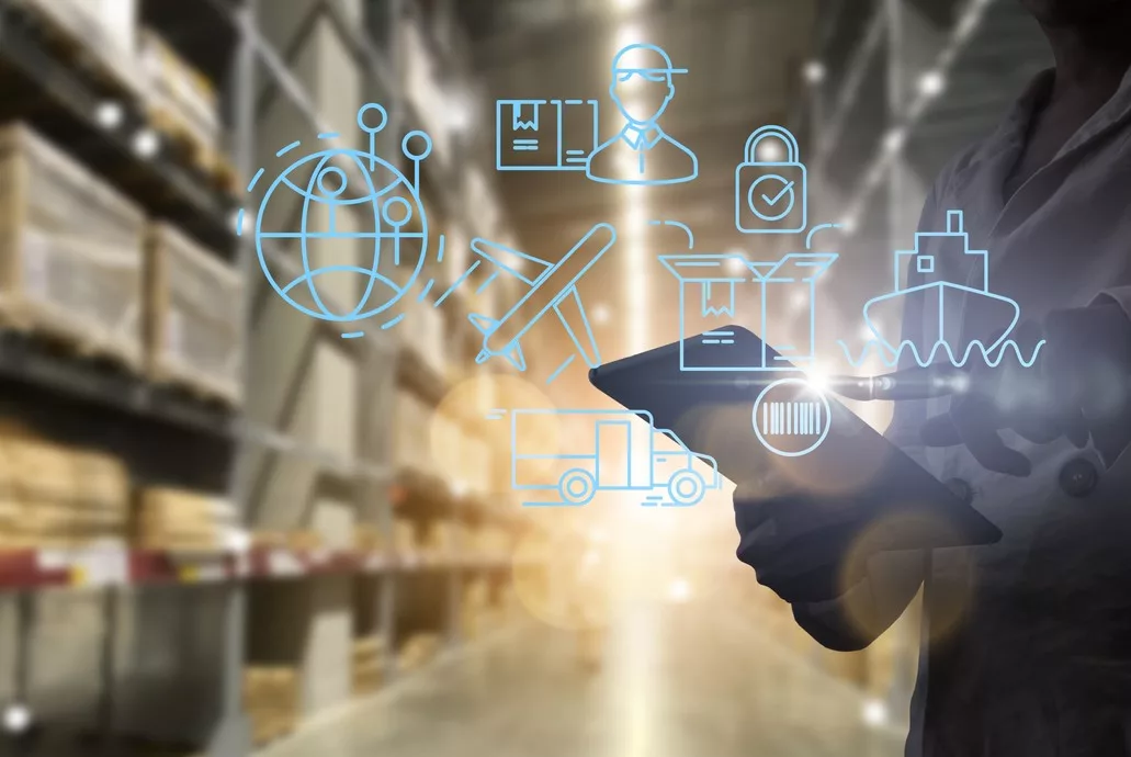 A PERSON HOLDS A TABLET COMPUTER IN A WAREHOUSE AISLE, SUPER-IMPOSED WITH SUPPLY CHAIN ICON GRAPHICS