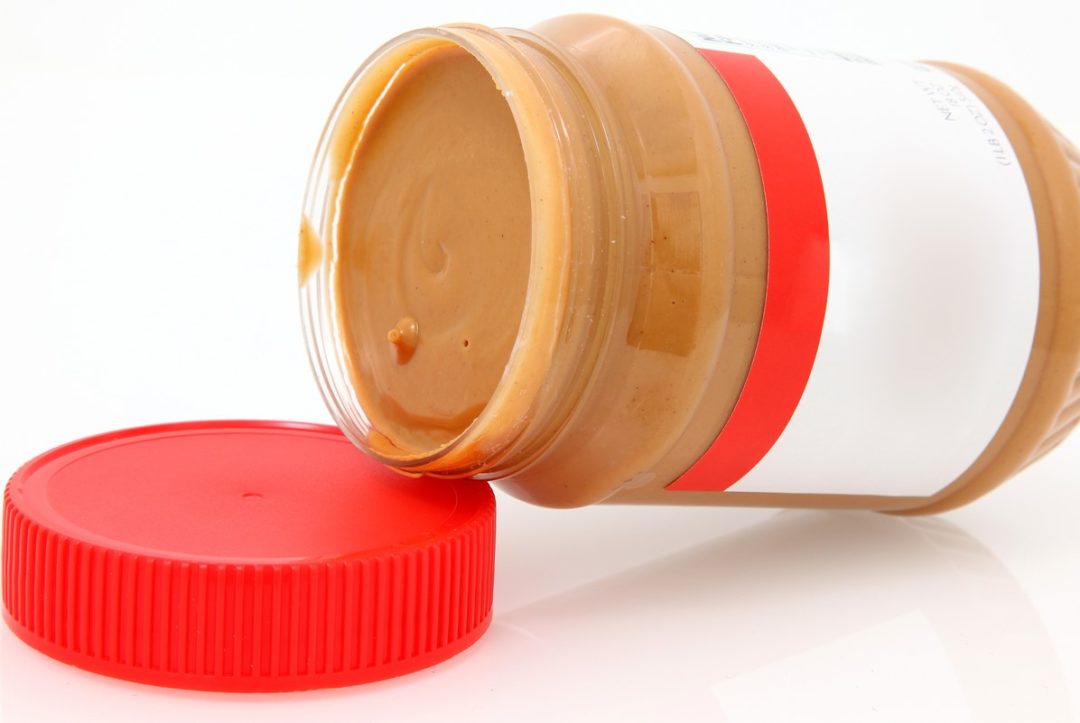 THE LIP OF AN OPEN JAR OF PEANUT BUTTER RESTS ON ITS LID