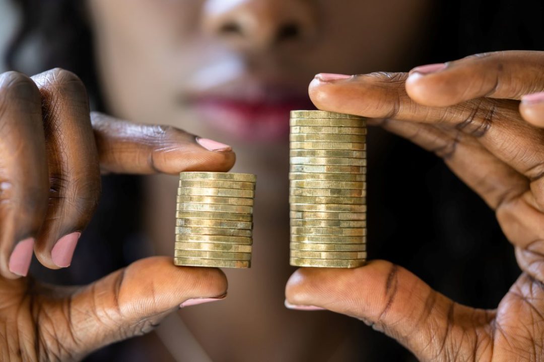 A WOMAN HOLDS UP TWO STACKS OF COINS, ONE SHORTER THAN THE OTHER.