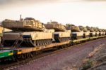 Light Brown Combat Ftrac 120mm Gun Tanks in Transport on Rail Train In Line with Blue Sky