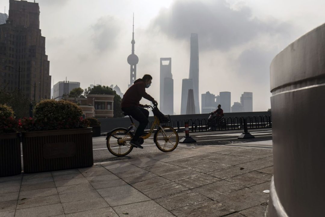 A BICYCLIST PASSES IN FRONT OF THE SHANGHAI SKYLINE