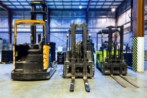 THREE FORKLIFTS SIT ON THE FLOOR OF A WAREHOUSE