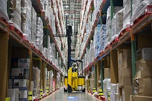 A WORKER OPERATES A FORKLIFT TRUCK IN A WAREHOUSE AISLE