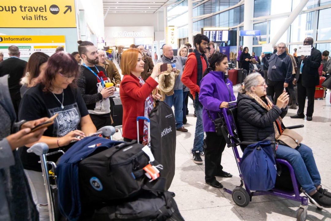 ARRIVING PASSENGERS PUSH LUGGAGE CARTS THROUGH A TERMINAL AT HEATHROW AIRPORT