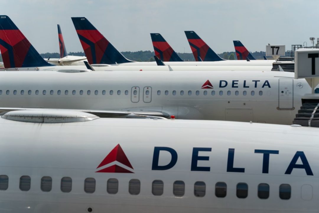 A ROW OF DELTA AIRPLANES SIT ON THE TARMAC AT AN AIRPORT