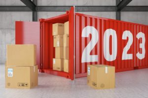 A BRIGHT RED SHIPPING CONTAINER PAINTED WITH YELLOW NUMERALS 2023 STANDS OPEN, REVEALING SHIPPING BOXES