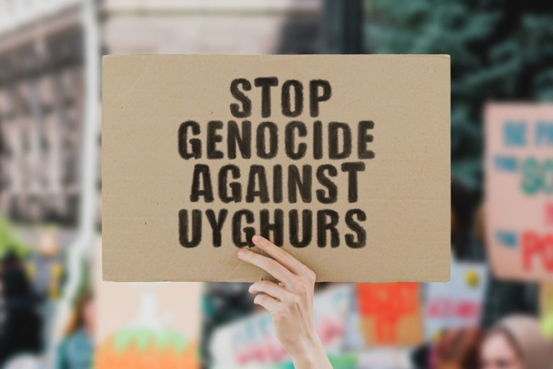 A HAND HOLDS UP A SIGN THAT READS STOP GENOCIDE AGAINST UYGHURS