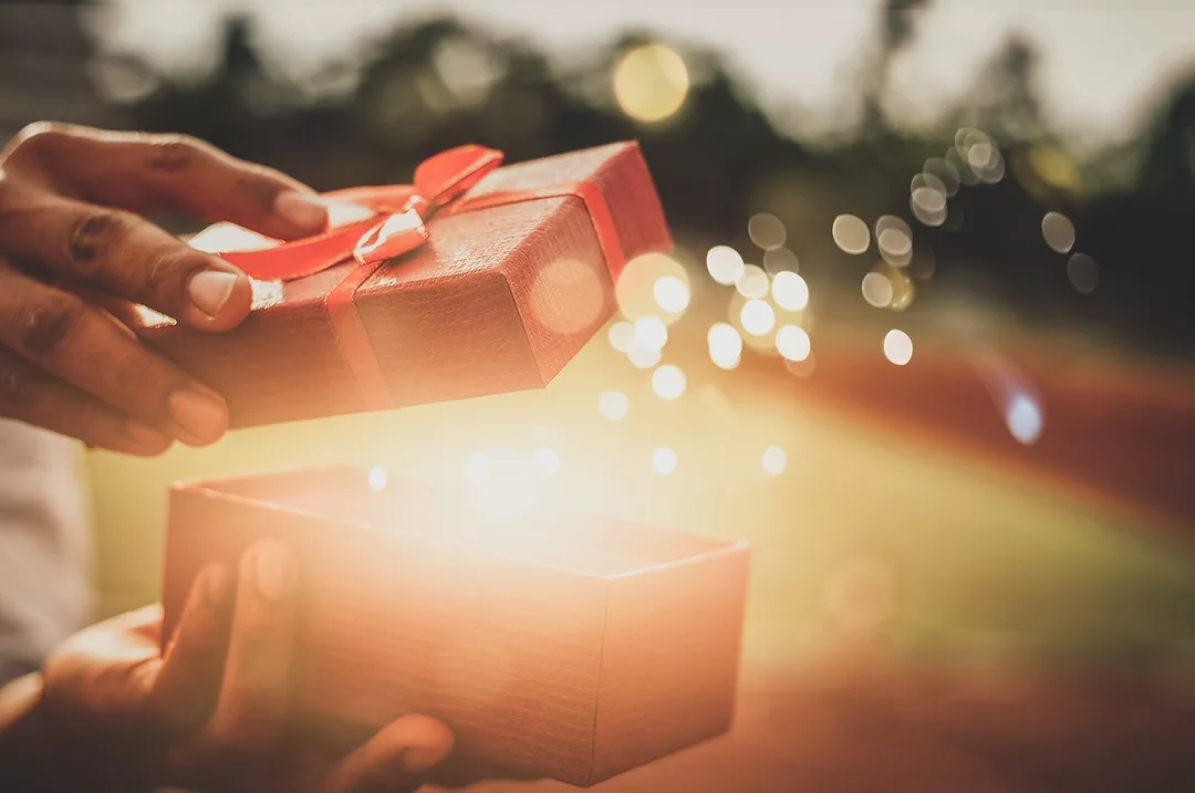 A HAND OPENS A GIFT BOX AND MAGIC SPARKLES EMERGE