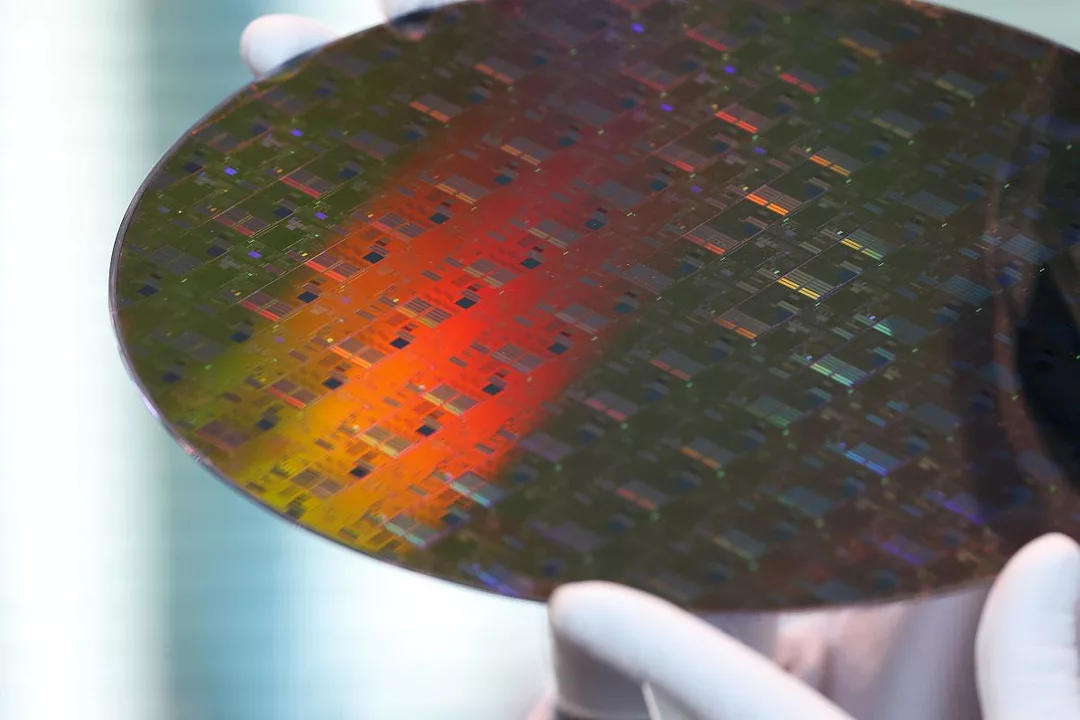 TWO HANDS IN RUBBER GLOVES HOLD A SEMICONDUCTOR CHIP DISK