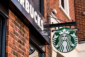 A STARBUCKS SIGN HANGS AGAINST A BRICK WALL OUTSIDE A STORE