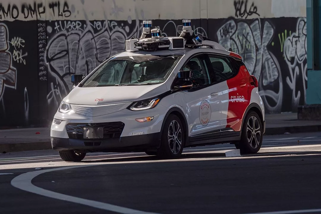 A WHITE CAR BEARING A RED STRIPE AND MULTIPLE PIECES OF EQUIPMENT ON ITS ROOF, DRIVES DOWN THE ROAD