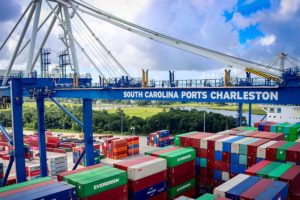 PHOTO OF PORT WITH SOUTH CAROLINA PORTS CHARLESTON WRITTEN ON A BLUE CRANE TOWERING OVER DOCKS FULL OF SHIPPING CONTAINERS