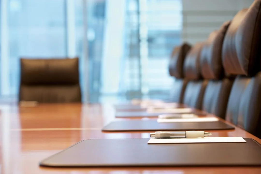 A SHORT FOCAL LENGTH PHOTO OF A LONG BOARDROOM TABLE, CLUSTERED BY EMPTY LEATHER CHAIRS