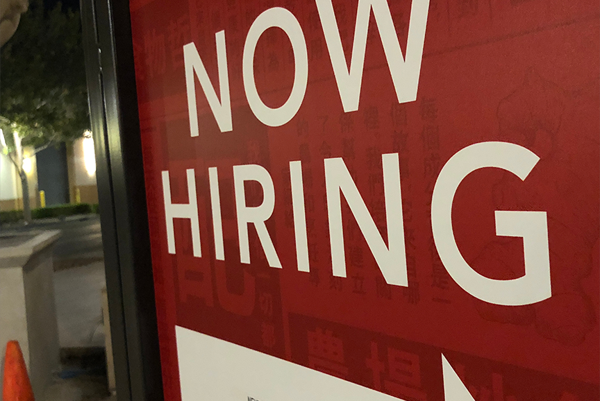 A SIGN IN A WINDOW READS NOW HIRING
