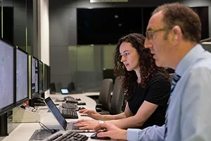 A MAN AND A WOMAN SIT AT ADJACENT COMPUTERS, ENGAGED IN THE SCREENS