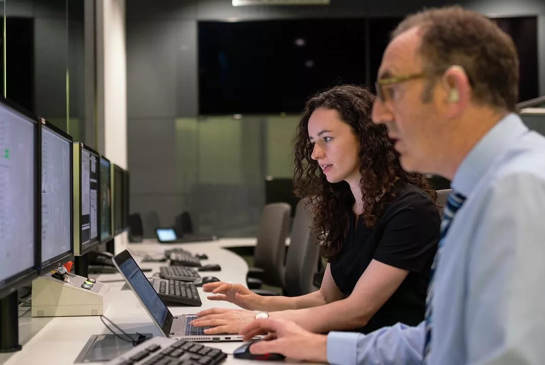 A MAN AND A WOMAN SIT AT ADJACENT COMPUTERS, ENGAGED IN THE SCREENS