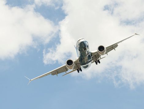 A BOEING 737 MAX, SEEN FROM BELOW, FLIES THROUGH A BLUE SKY WITH CLOUDS