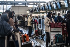 MASKED TRAVELERS PUSHING LUGGAGE CARTS CROWD A CHINESE AIRPORT CHECK IN