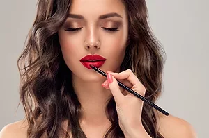AN ELEGANT HAND APPLIES LIPSTICK WITH A BRUSH TO A GLAMOROUS WOMAN'S FACE