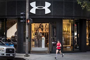  A RUNNER JOGS PAST AN OPEN STORE BEARING THE UNDER ARMOUR LOGO