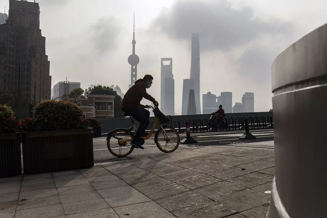 A BICYCLIST RIDES BENEATH THE SHANGHAI SKYLINE