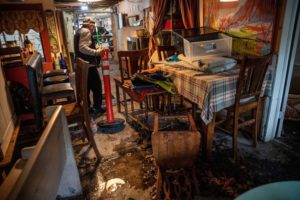 A MAN DRAGS A HAZARD POLE THROUGH A FURNISHED, FLOODED ROOM