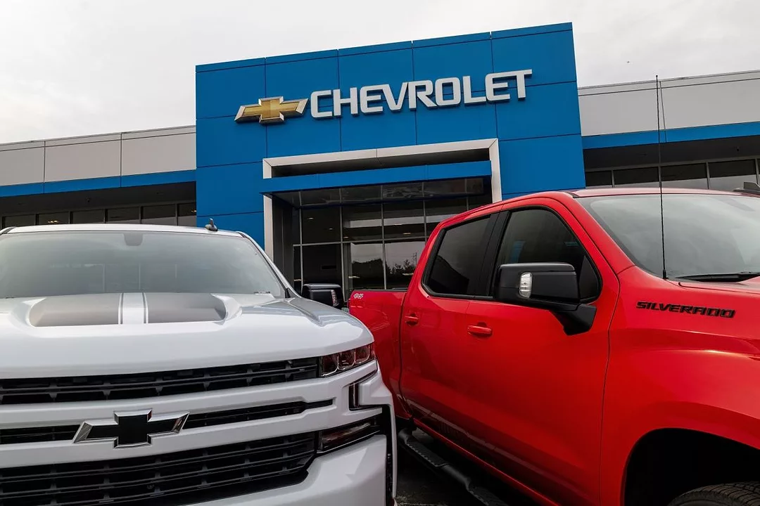 A SILVER AND A RED VEHICLE STAND SIDE BY SIDE, BEARING THE GM LOGO