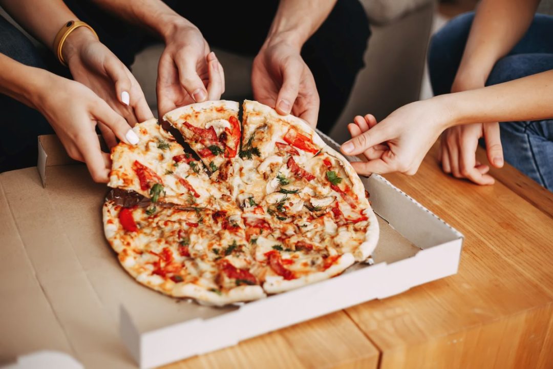 MANY HANDS BREAK APART A FRESHLY STEAMING PIZZA