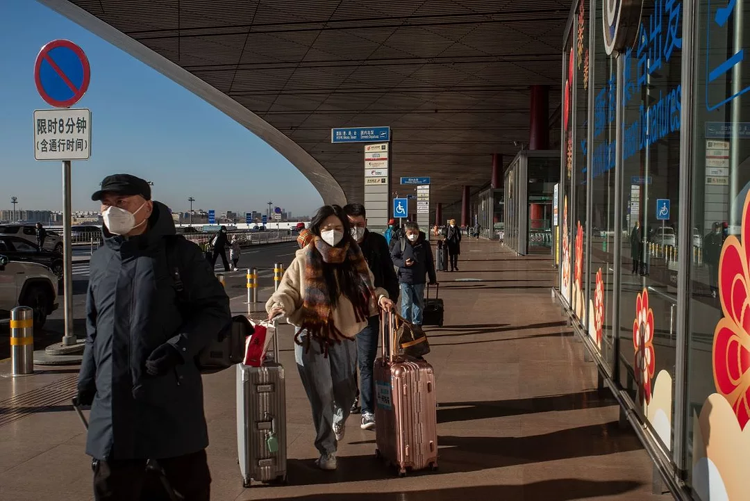 People push their luggage outside an airport, wearing masks.
