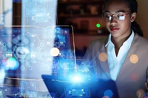 A WOMAN SITS AT A COMPUTER SURROUNDED BY LINES OF LIGHT