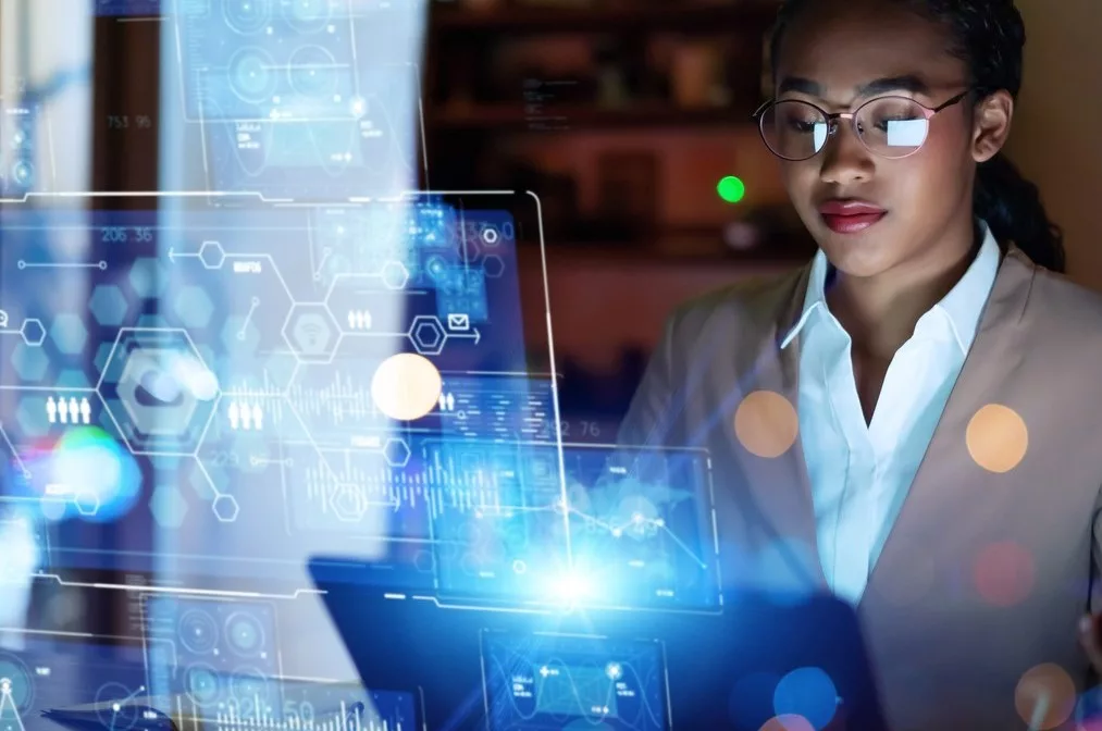 A WOMAN SITS AT A COMPUTER SURROUNDED BY LINES OF LIGHT