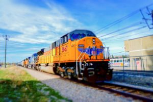 A BRIGHT ORANGE TRAIN WITH THE BLUE AND RED UNION PACIFIC LOGO PROCEEDS ALONG TRACKS UNDER A BLUE SKY