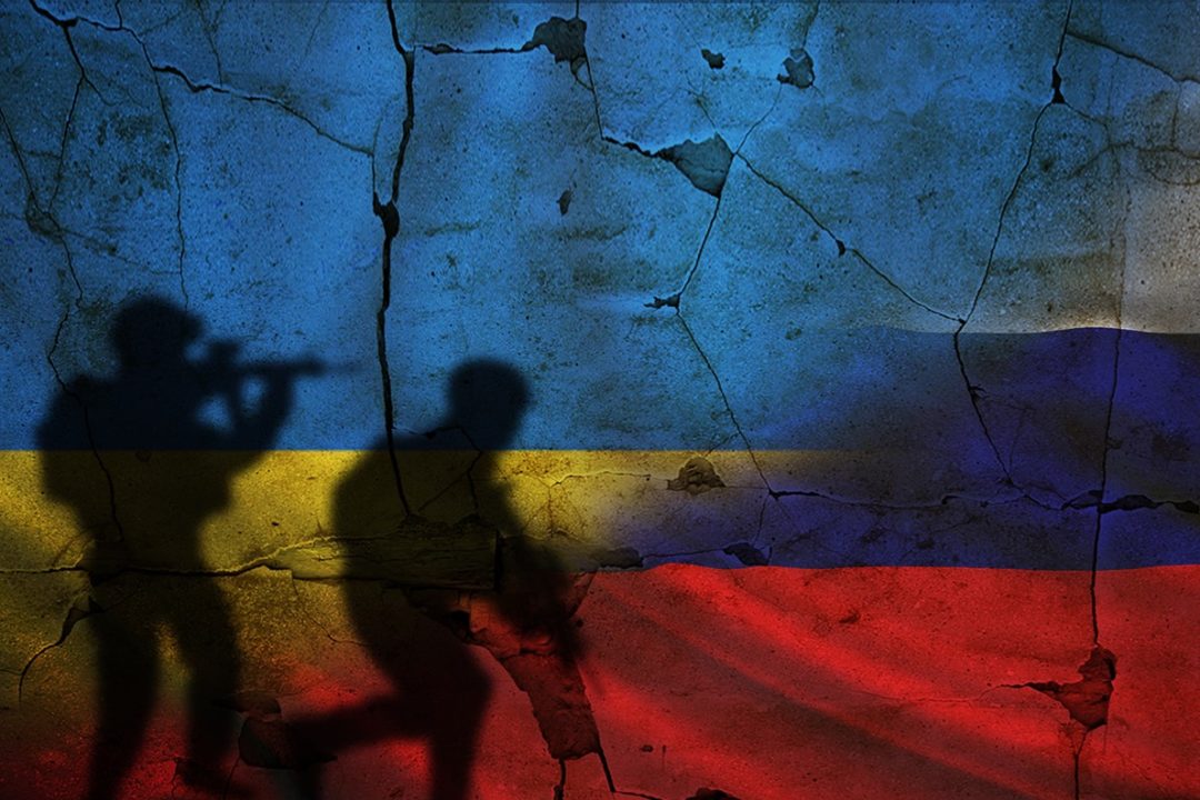 THE SHADOWS OF ARMED SOLDIERS PASS OVER A CRACKED CONCRETE WALL PAINTED WITH THE COLORS OF THE UKRAINIAN FLAG