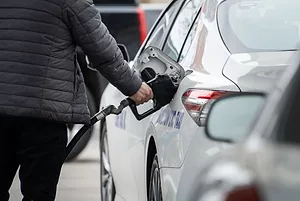 A FIGURE IN A DOWN JACKET FILLS A CAR AT A GAS PUMP 
