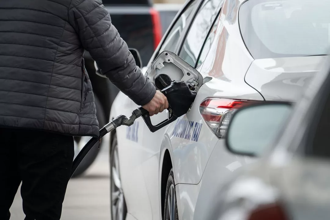 A FIGURE IN A DOWN JACKET FILLS A CAR AT A GAS PUMP 