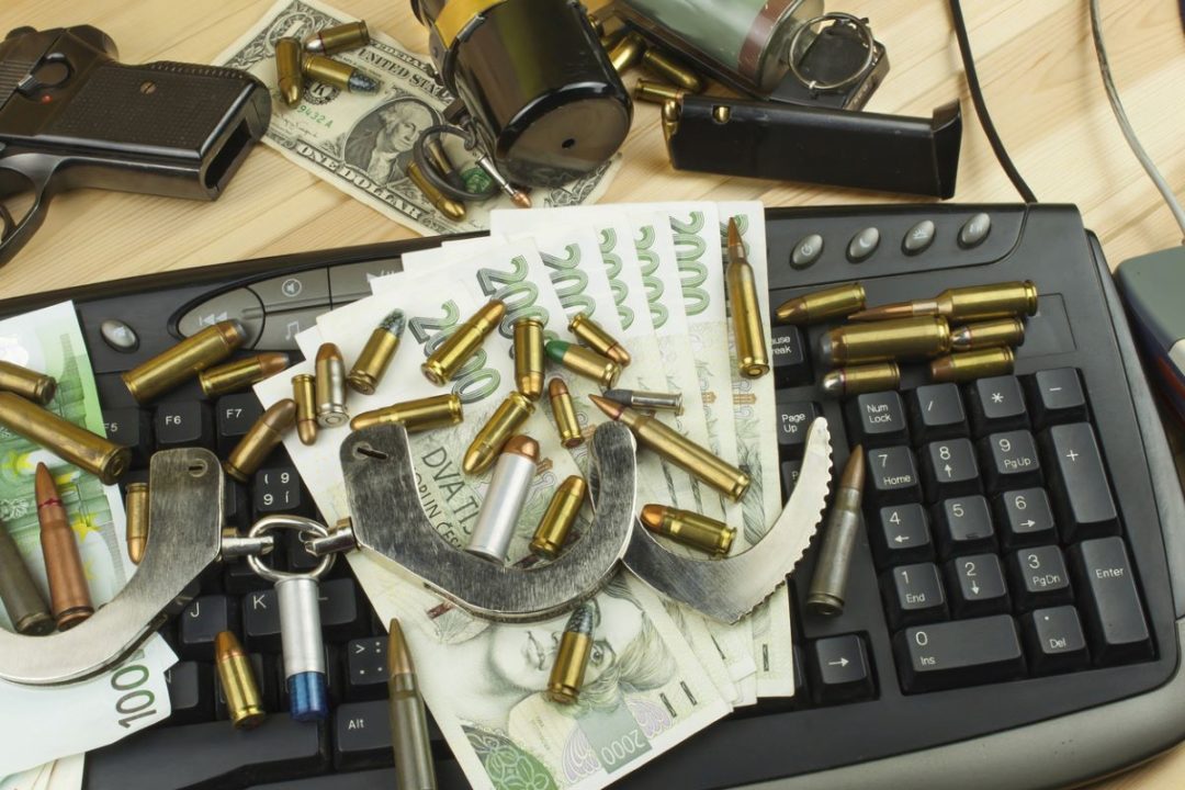 A COMPUTER KEYBOARD IS LITTERED WITH CASH, HANDCUFFS AND BULLETS