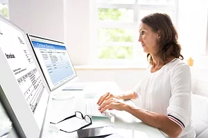 A WOMAN TYPES AT A COMPUTER SHOWING INVOICING