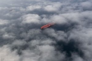 A HIGH AERIAL SHOT OF AN OIL TANKER ON THE OCEAN, SEEN THROUGH CLOUDS