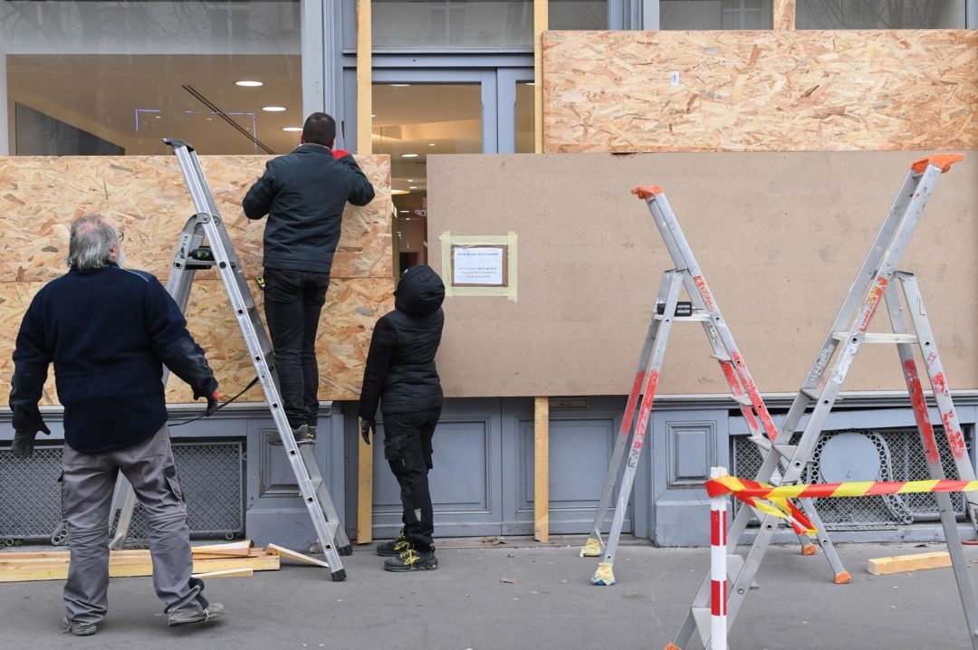 MEN ON LADDERS ATTACH PARTICLE BOARD TO STORE WINDOWS