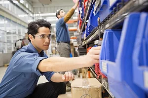 A WORKER CROUCHES TO PICK AND ORDER IN A WAREHOUSE AISLE